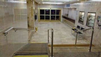 Um saguão de hotel com piso de mármore, um balcão de recepção e uma escadaria com corrimãos de metal.