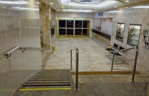 A hotel lobby with marble flooring, a reception desk, and a staircase with metal railings.