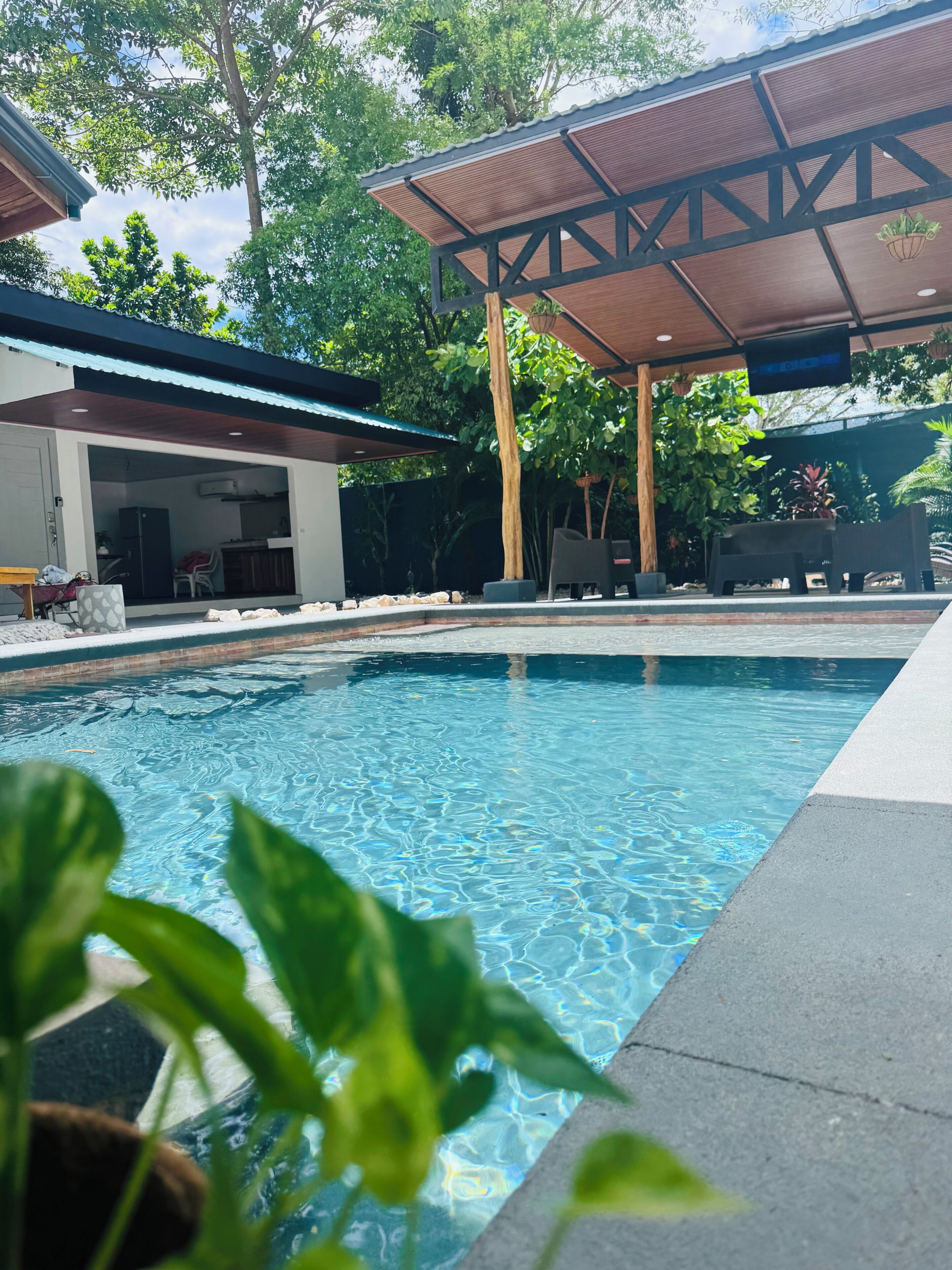 A swimming pool with a wooden deck and a covered seating area.