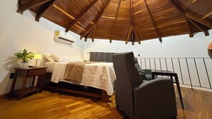 Une chambre à coucher avec un plafond en bois, un lit, une table de chevet, une chaise et une petite table avec une lampe.