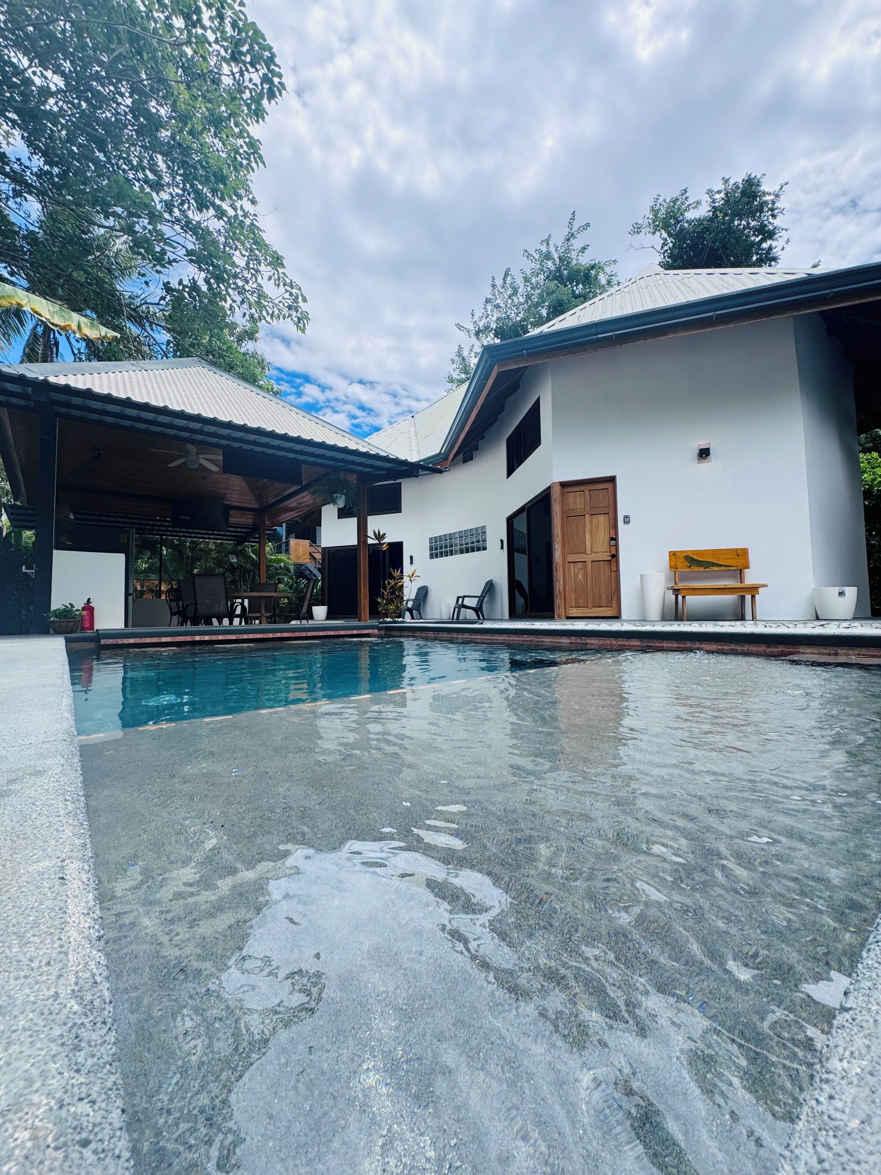 A swimming pool area with a covered seating area and a building with a white exterior.