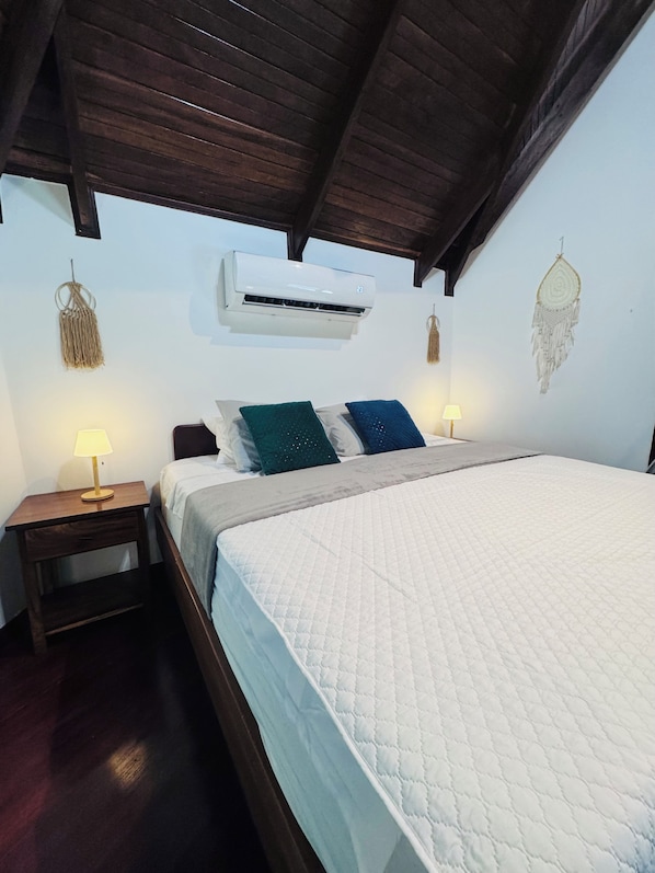 A bedroom with a bed, bedside tables, an air conditioning unit, and wall decorations.