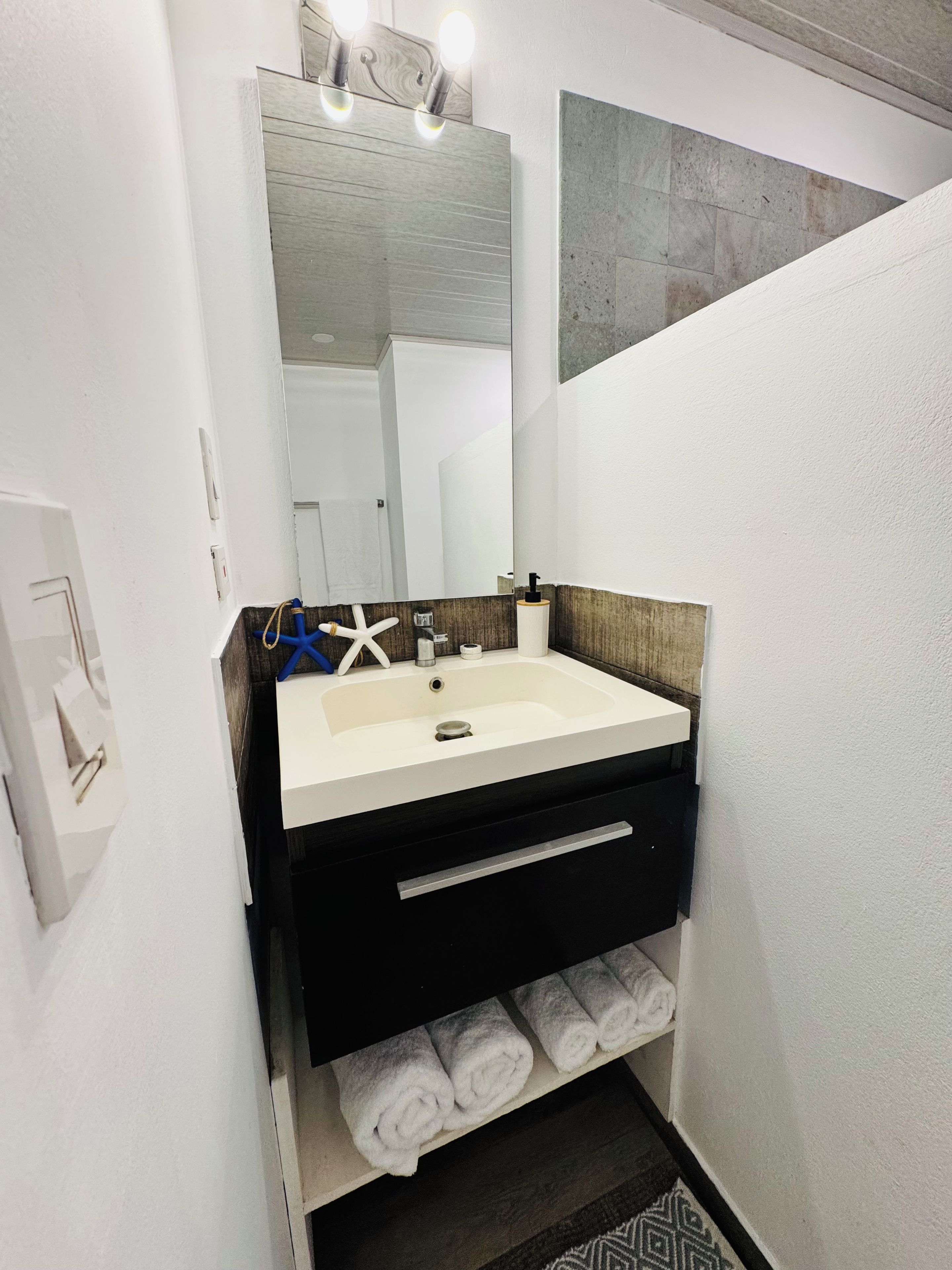 Un baño moderno con un lavabo blanco, tocador de madera oscura y un espejo arriba.