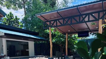 A swimming pool with a covered patio area, a building with a glass door, and surrounding greenery.