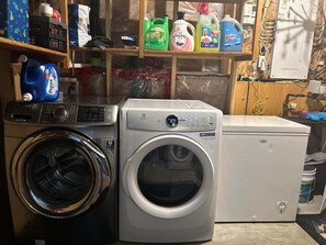 A laundry area with a front-loading washing machine, a dryer, and various cleaning supplies on shelves. - Home Sweet Home in Red Deer  Alberta!!
We offer 5 bedrooms for your family stay! (Red Deer)