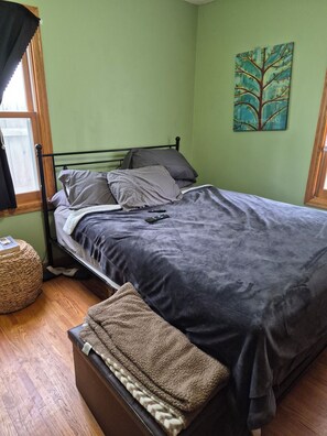 Una camera da letto con un letto, cuscini, una coperta, un quadro appeso al muro e una finestra con tende.