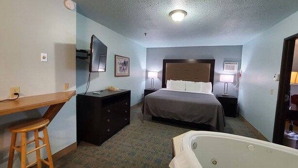 Una camera d'albergo con un letto, una scrivania, una sedia, un comò, una televisione, due lampade da comodino e una vasca da bagno.
