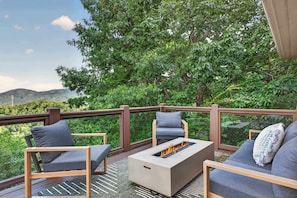 Terraza exterior con una chimenea, asientos y vistas a un área boscosa.