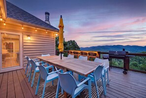 An outdoor deck with a wooden table and blue chairs, a grill, and a view of mountains. - 6BR Mountain Getaway  Pool  Hot Tub  Game Room (Black Mountain)