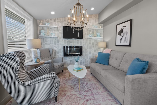 A living room with a television, a chandelier, a sofa, and patterned chairs.