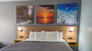 Una camera d'albergo con un letto grande, due comodini e tre quadri appesi al muro raffiguranti scene naturali.