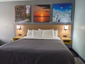 A hotel room with a large bed, two bedside tables, and three wall-mounted paintings depicting nature scenes. - Relaxing Whirlpool Retreat Near Tawas Bay & Michigan's Scenic Shoreline (Tawas City)