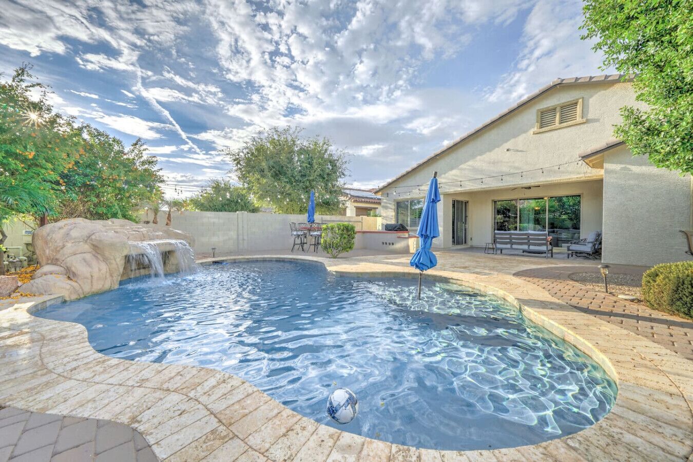 A swimming pool with a waterfall feature, surrounded by a patio area with outdoor furniture and umbrellas.
