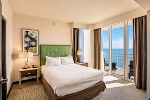 Habitación de hotel con cama, mesita de noche, lámpara, un cuadro y balcón con vista al mar.