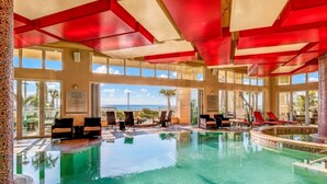 An indoor swimming pool with clear blue water, surrounded by lounge chairs and a view of the ocean. - Virginia Beach | Oceanfront Beach Retreat | Pool & Beach | 2BR (Virginia Beach)
