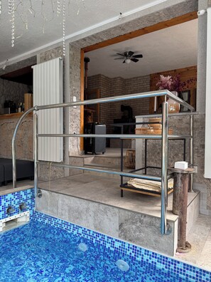 A swimming pool with a metal ladder, a ceiling fan, and a rustic interior with stone walls and wooden beams. - Vrbo Property (Gornji Orašac)