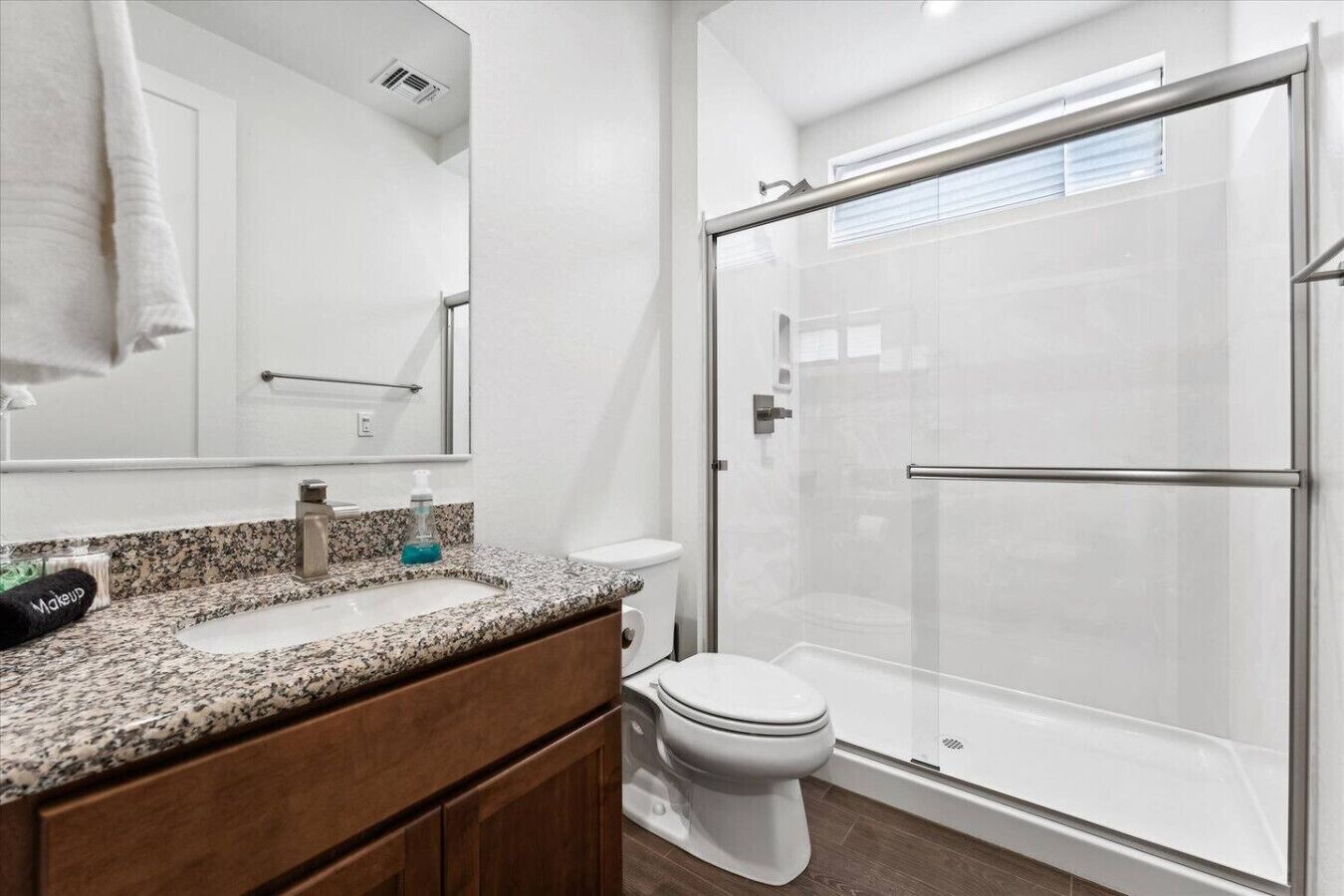 Een moderne badkamer met een granieten aanrechtblad, een wit toilet en een douchecabine met glazen wanden.