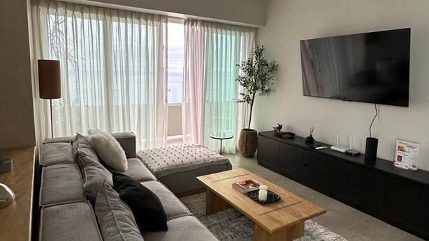 A modern living room with a grey sofa, a round coffee table, and a flat-screen TV mounted on the wall. - Vrbo Property (Tijuana)