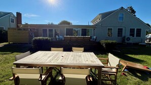 Ein Garten mit Holztisch und -stühlen, einer überdachten Terrasse und einem Haus mit Schornstein.
