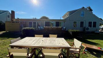 Un pati posterior amb una taula i caires de fusta, una zona de porxo coberta i una casa amb una xemeneia.