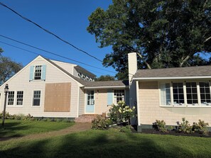 A two-story house with a front porch, a brick staircase, and a large tree in the background. - Designer renovated 4-bedroom house in coveted Bonnet Shores with AC (Narragansett)