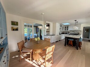 A modern kitchen with white cabinets, a marble countertop, and a dining area with wicker chairs and a wooden table. - Designer renovated 4-bedroom house in coveted Bonnet Shores with AC (Narragansett)