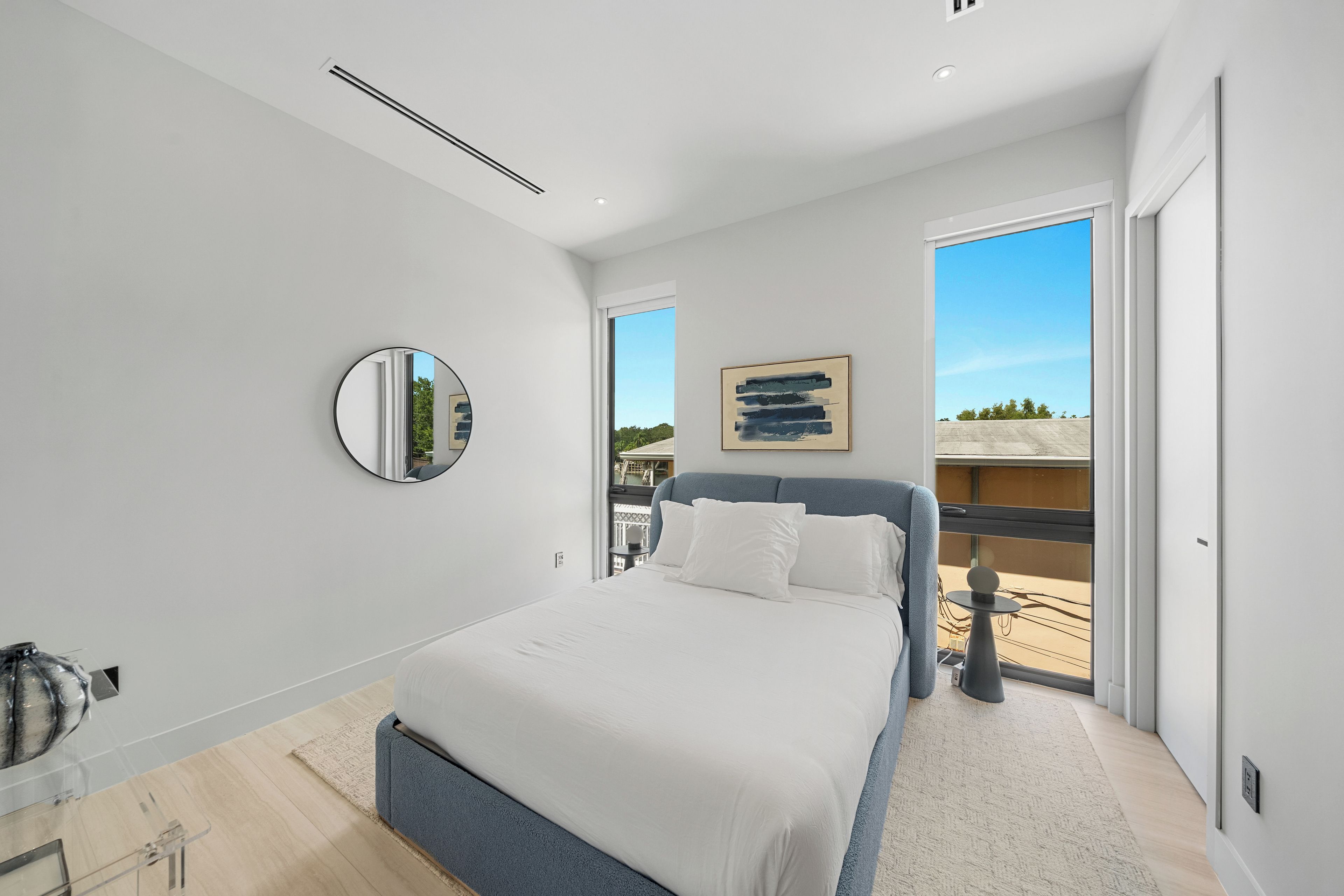A modern bedroom with a large bed, a round mirror, and a view of the outdoors through a sliding door.