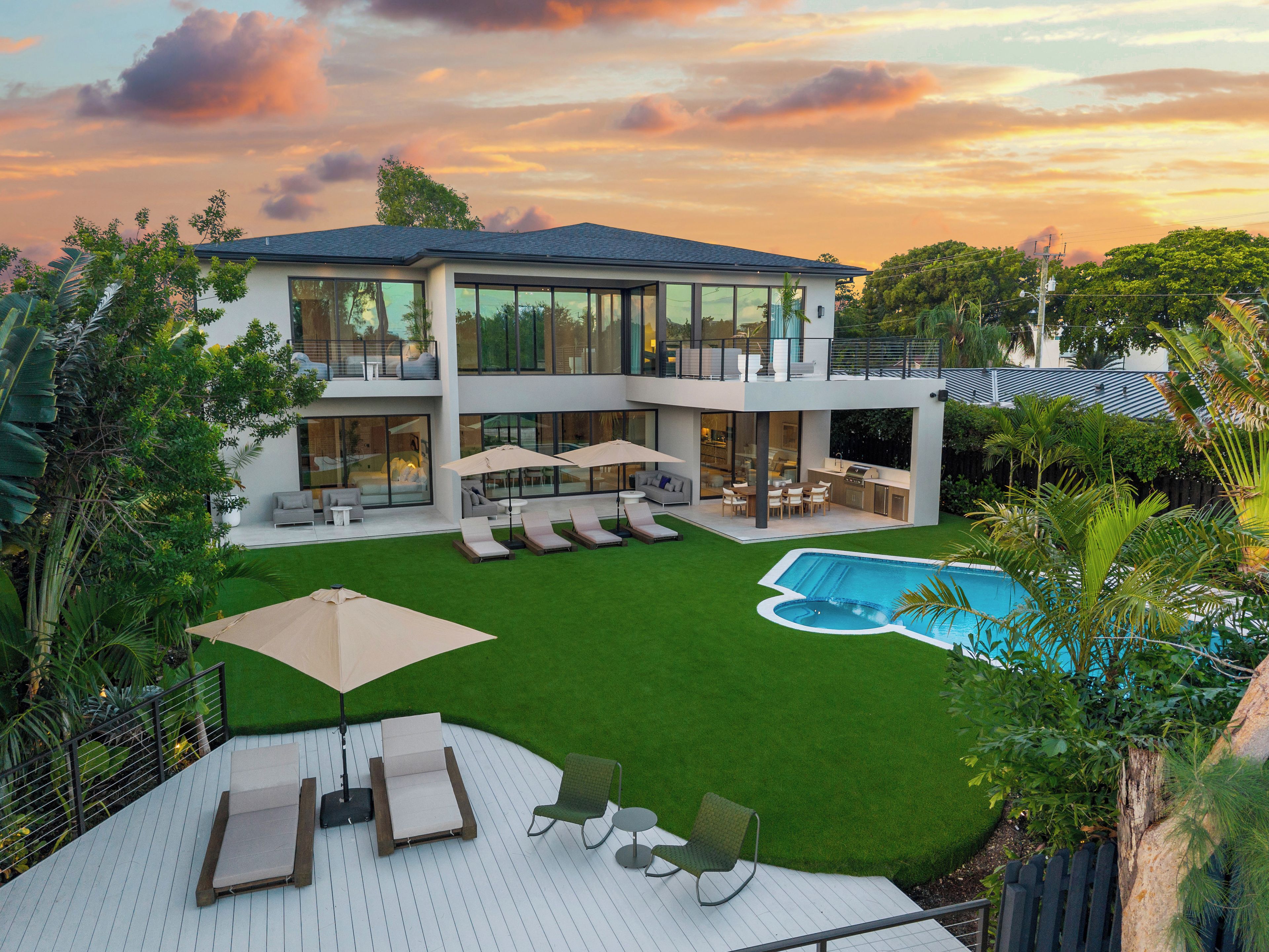 A modern two-story house with a swimming pool, outdoor seating, and lush greenery.