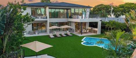 A modern two-story house with a swimming pool, outdoor seating, and lush greenery.