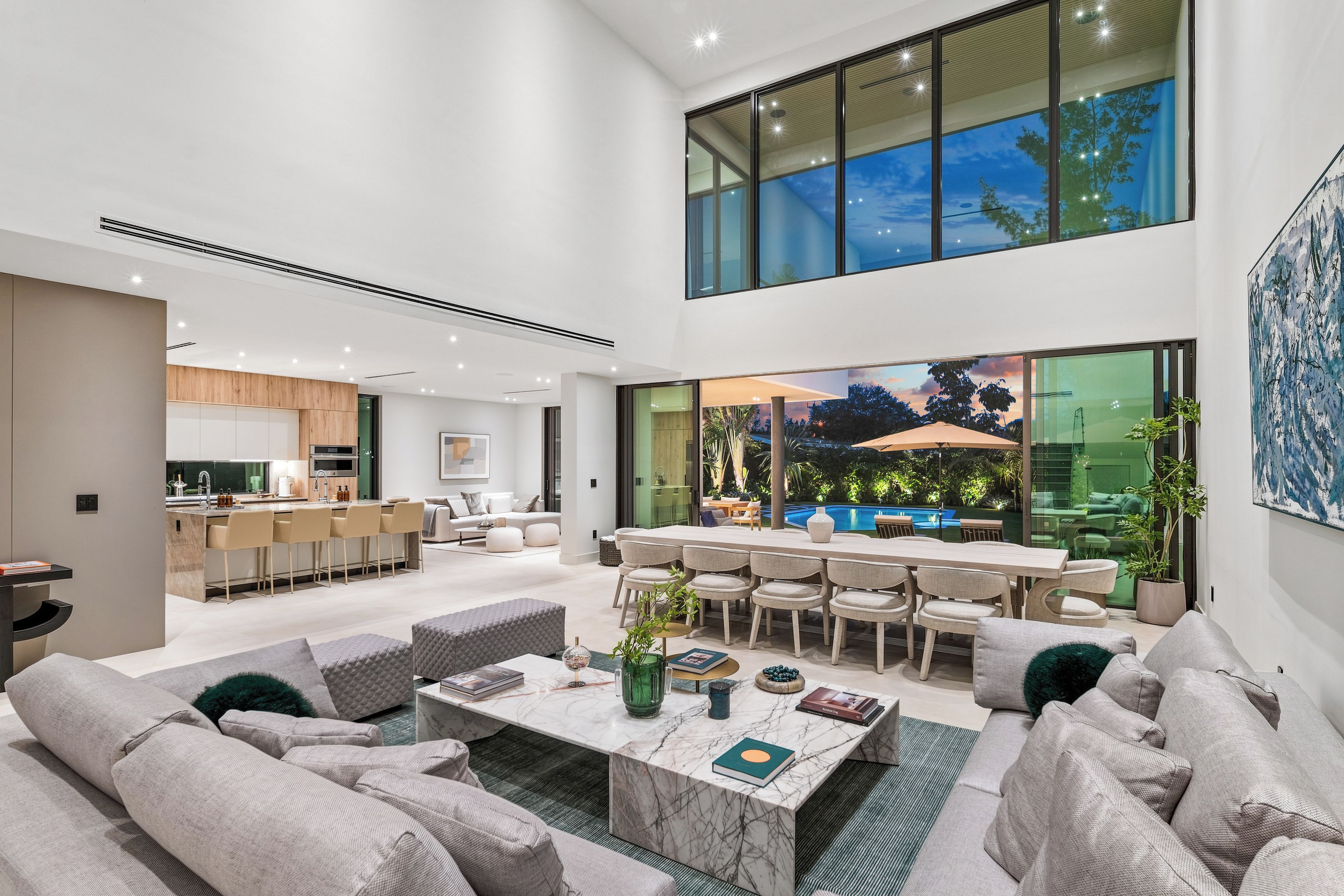 A spacious living area with a high ceiling, a dining area with a view of the outdoors, and a kitchen with modern appliances.