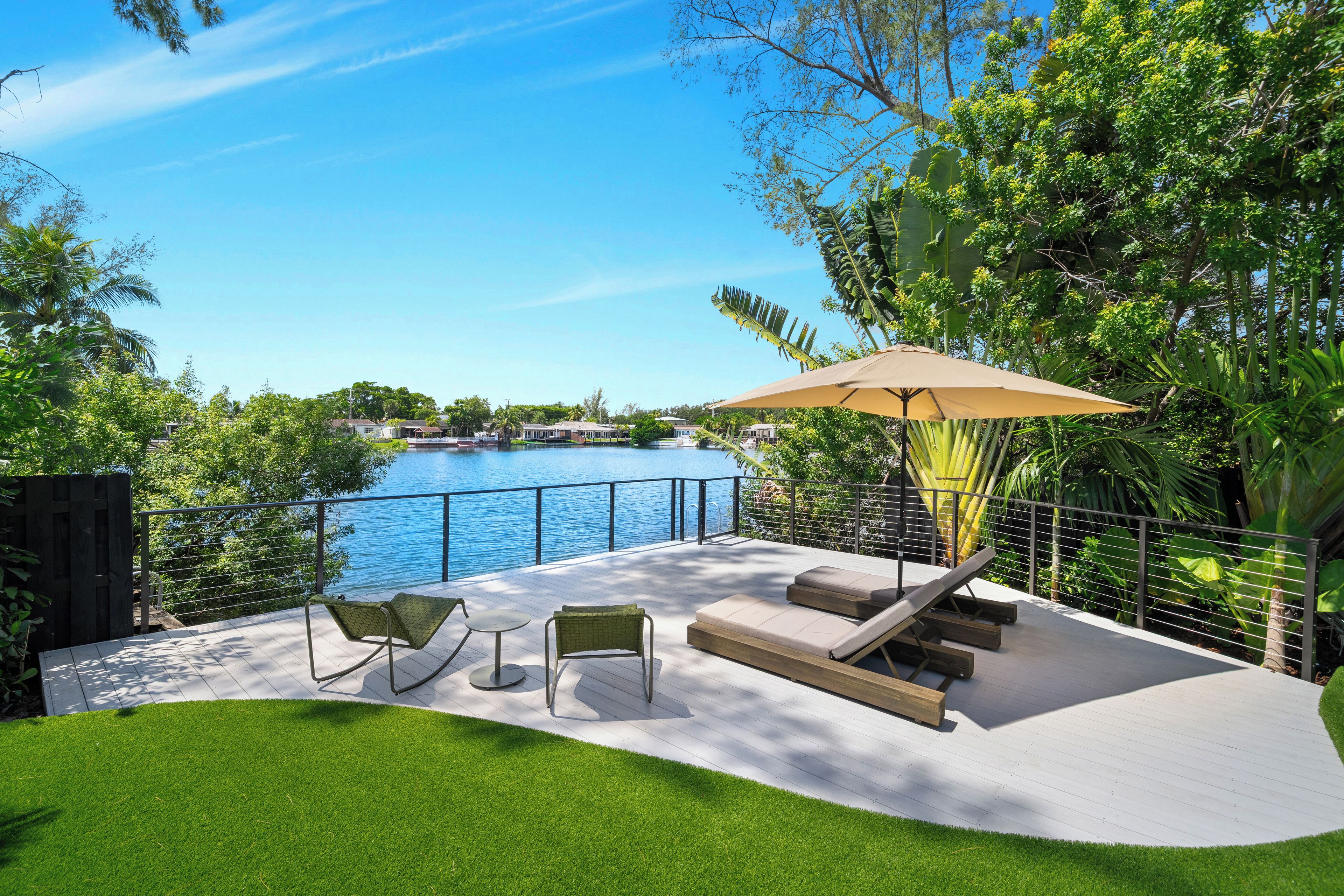 A deck with outdoor furniture overlooking a body of water, surrounded by lush greenery.