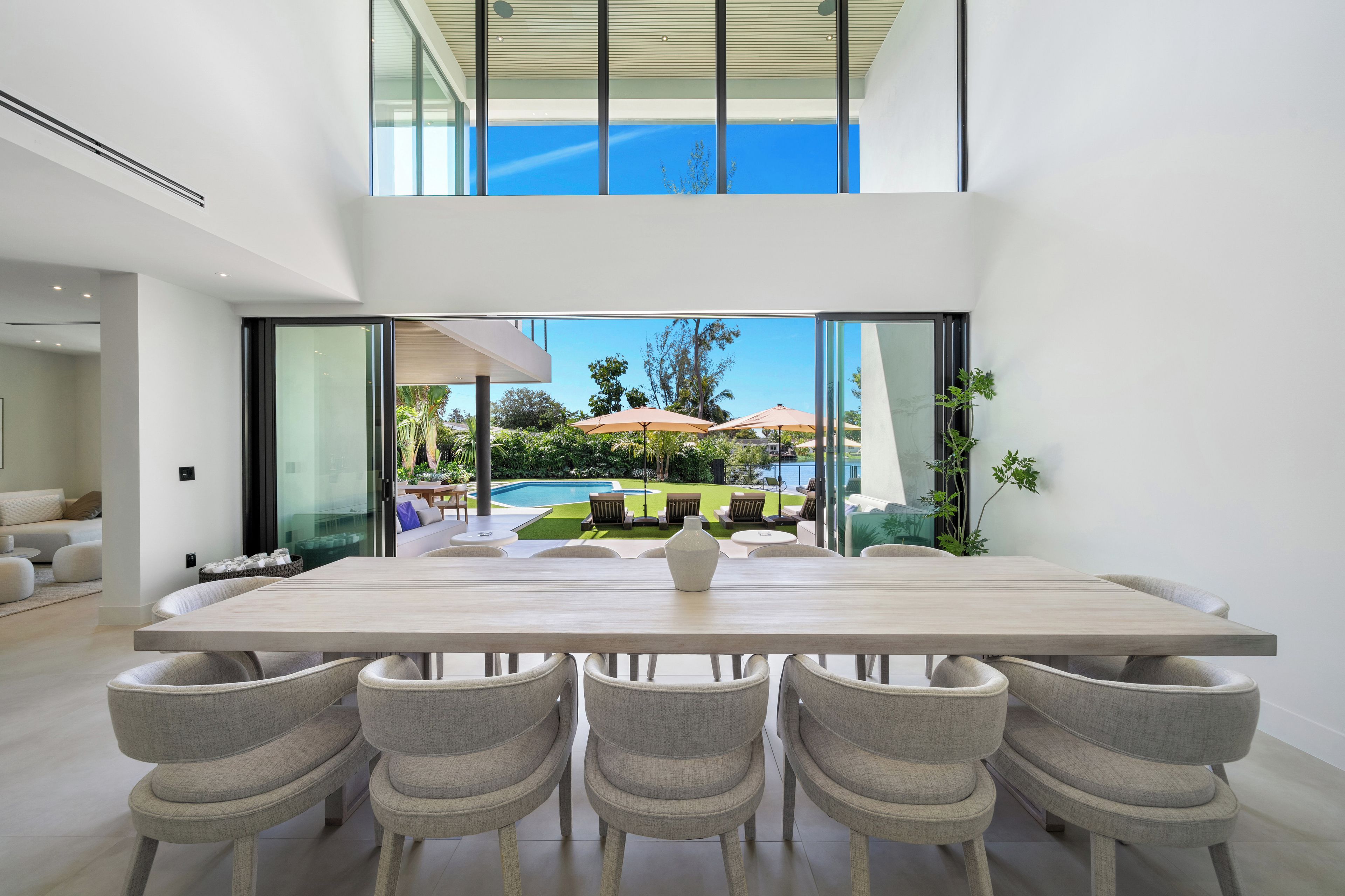A modern dining area with a large table and six chairs, overlooking a pool and outdoor seating.