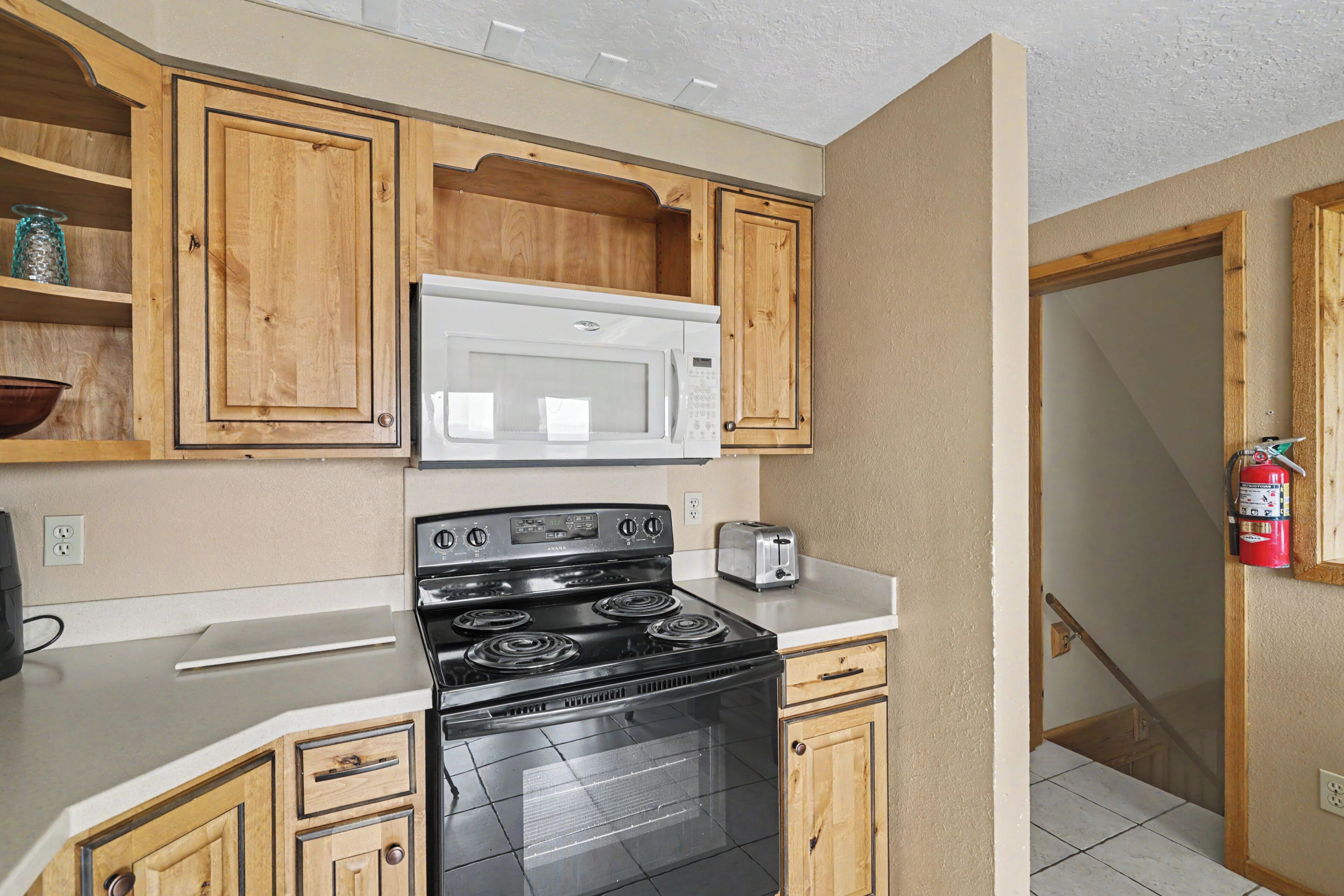 A compact kitchen with wooden cabinets, a stainless steel stove, a microwave, and a toaster.