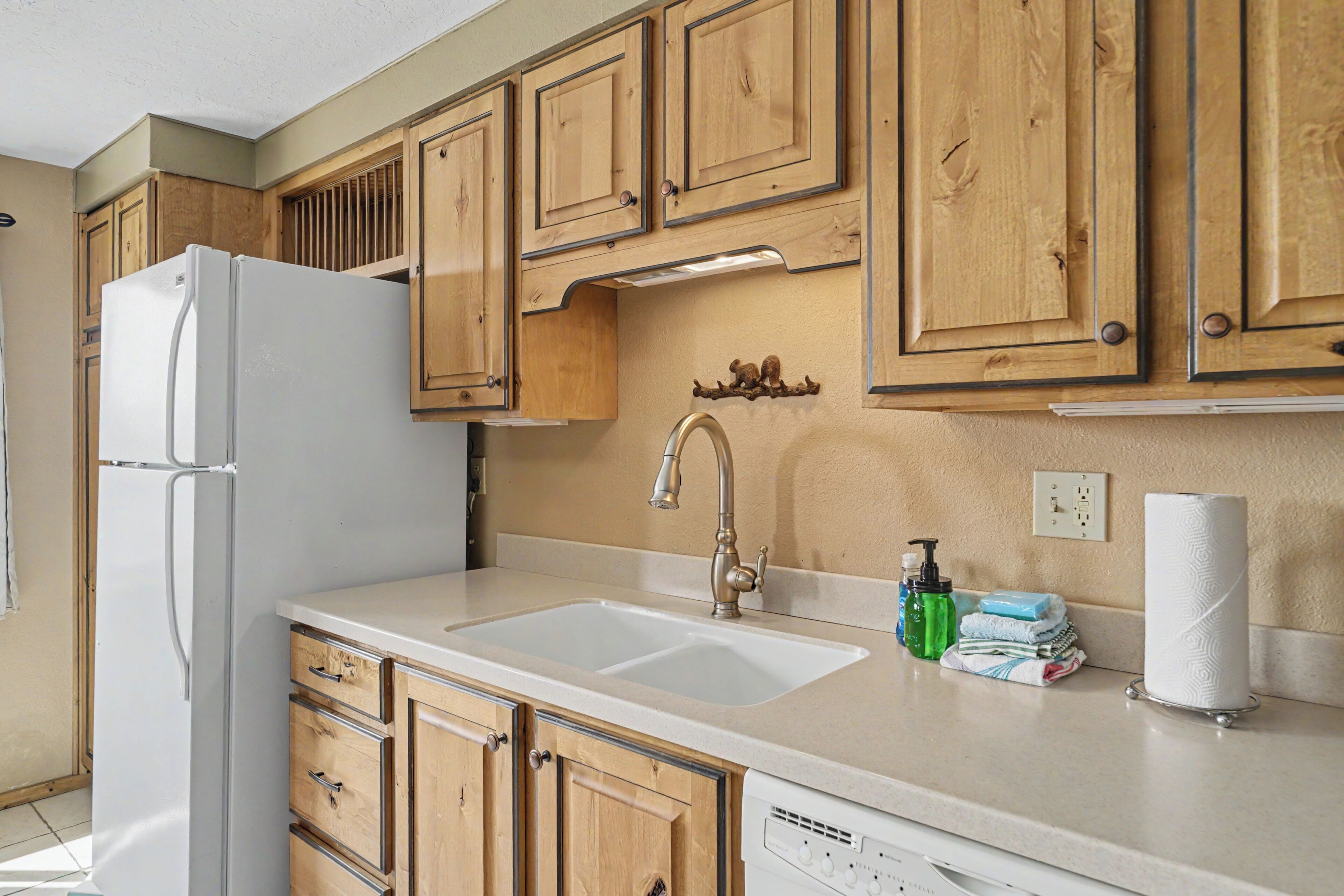 A kitchen with wooden cabinets, a white refrigerator, a sink with a faucet, and a dish rack with towels.