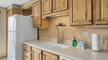 A kitchen with wooden cabinets, a white refrigerator, a sink with a faucet, and a dish rack with towels.