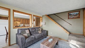 A living room with a gray sofa, wooden coffee table, and a staircase leading to a kitchen.