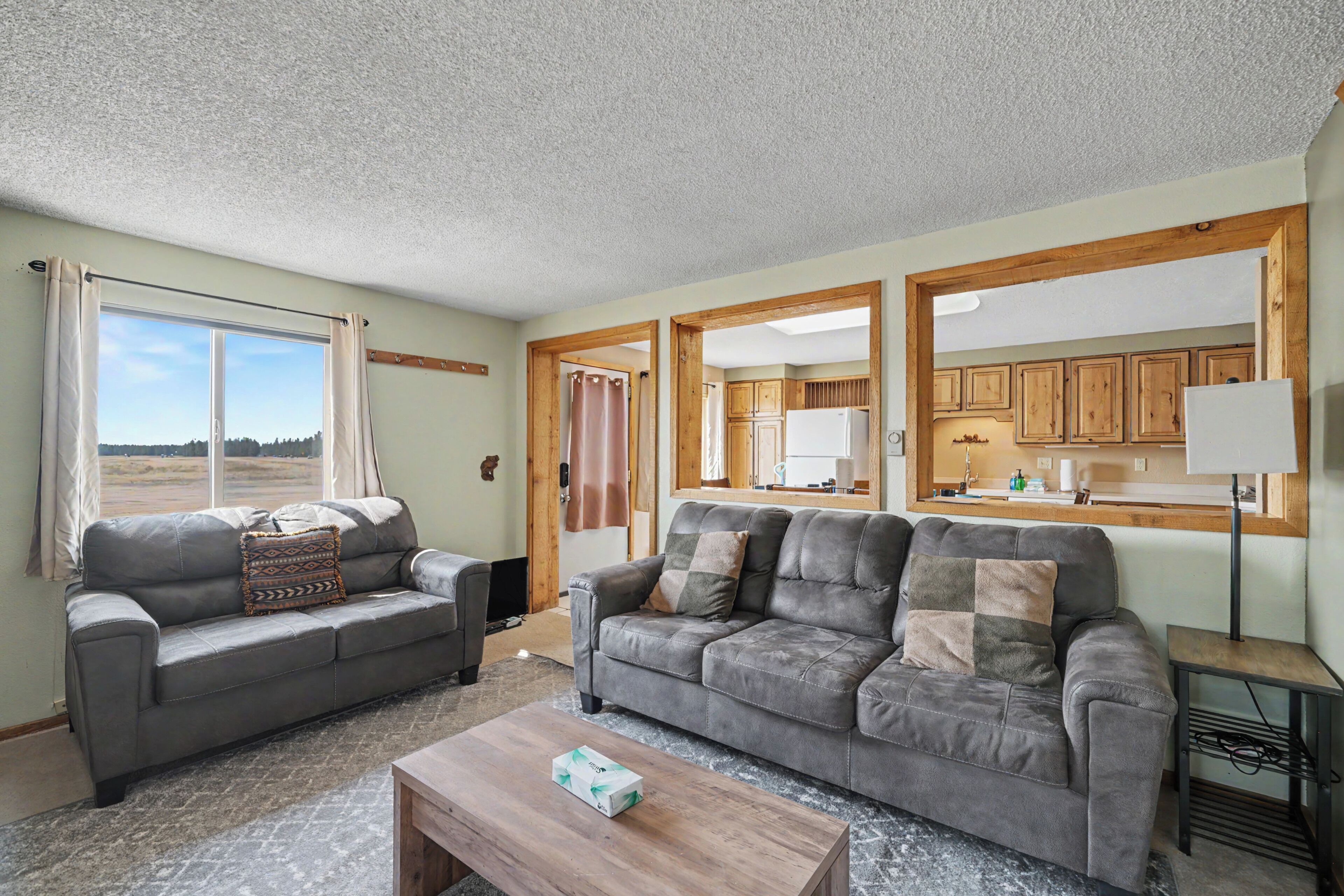 A living room with two grey sofas, a wooden coffee table, and a view of the kitchen through an open doorway.