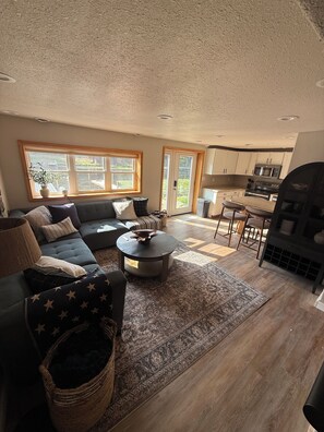 A living room with a sofa, a coffee table, and a rug. There is a kitchen area with cabinets and a microwave. - Cozy Lakefront Cottage — Private Dock & Fire Pit (Woodruff)