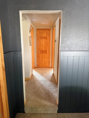 A hallway with a wooden door at the end, carpeted floor, and walls with a textured finish. - Cozy Lakefront Cottage — Private Dock & Fire Pit (Woodruff)