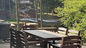 Eine Außenpatio mit einem Holztisch und Bänken, umgeben von Bäumen und Blick auf ein Gebäude im Hintergrund.
