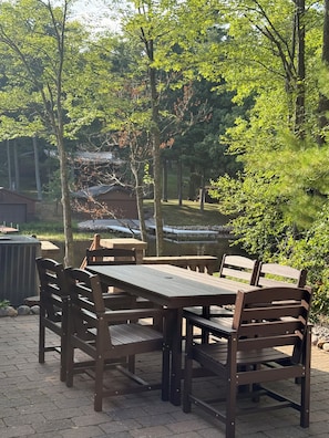 Une terrasse extérieure avec une table et des bancs en bois, entourée d’arbres et offrant une vue sur un bâtiment en arrière-plan.