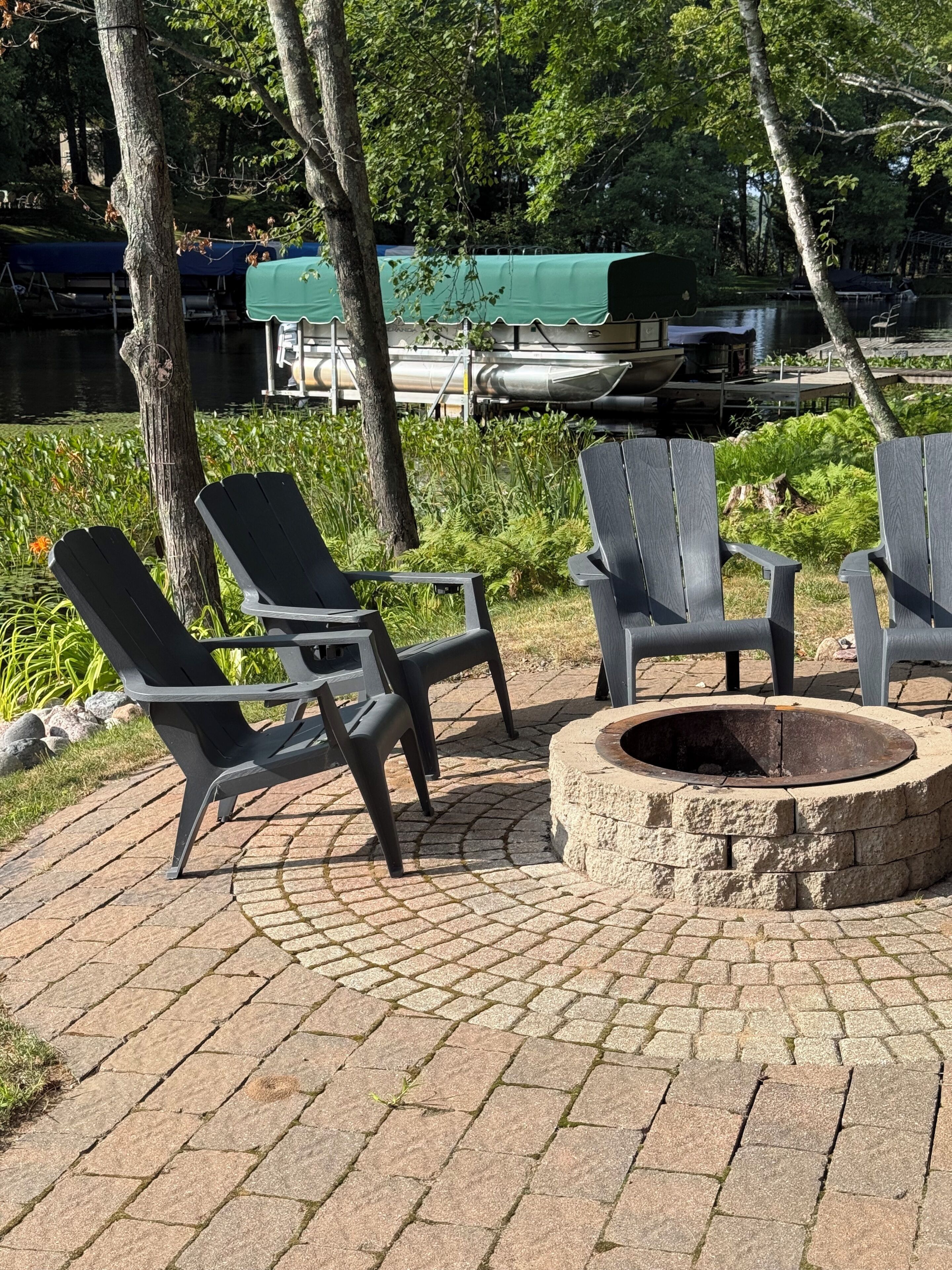 An outdoor seating area with Adirondack chairs and a stone fire pit.