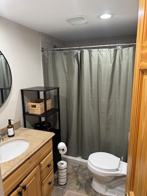Une salle de bain avec un lavabo blanc, une étagère noire avec des paniers, des toilettes et un rideau de douche.