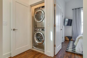 A laundry room with two front-loading washing machines, a television mounted on the wall, and a bed with a checkered rug. - City Views In Hillsboro Village for 24 Guests, Garage, Walk to Vanderbilt And Boutique Shopping (Nashville)
