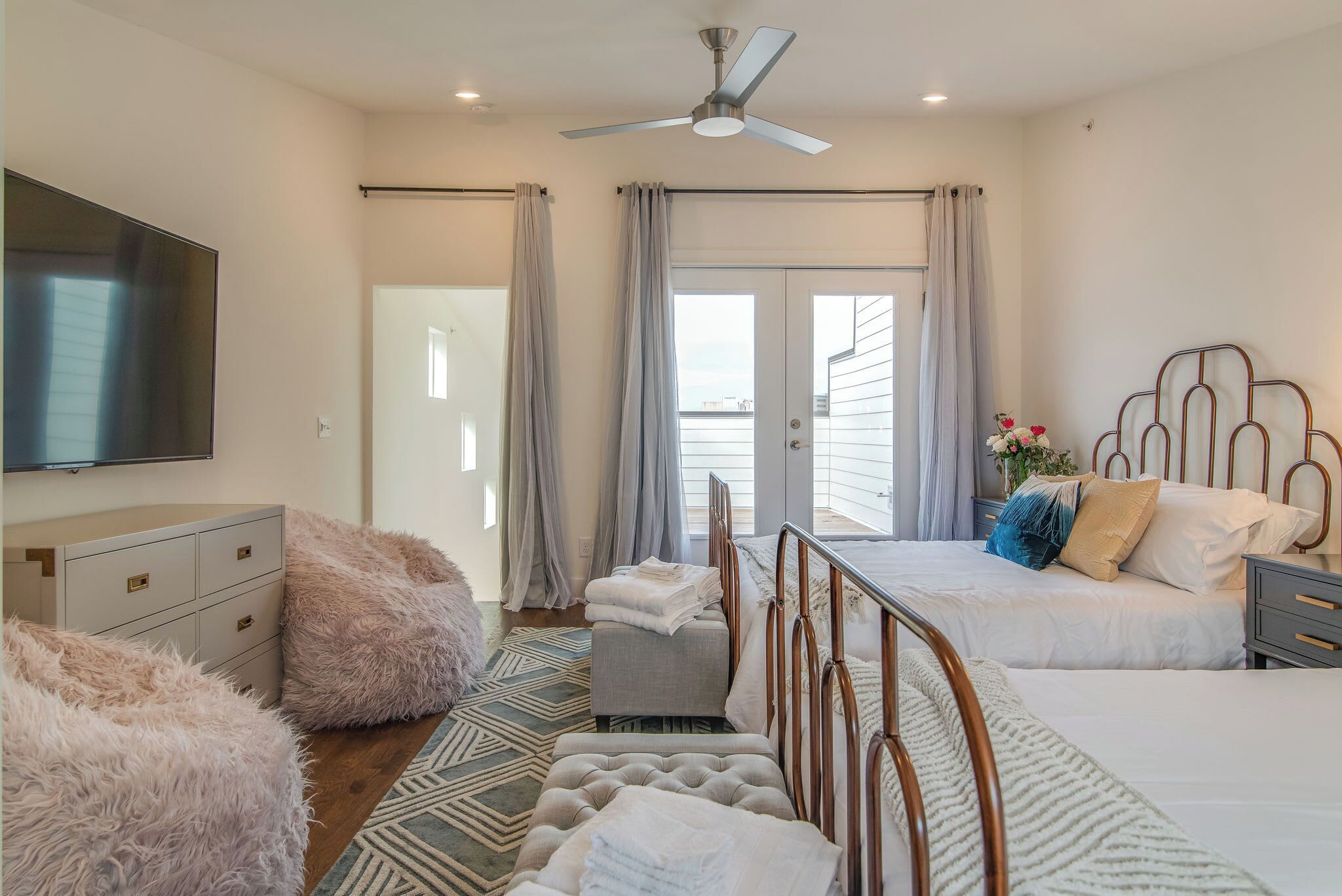A bedroom with a bed, a bedside table, a TV, a ceiling fan, and a view of the outside.