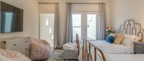 A bedroom with a bed, a bedside table, a TV, a ceiling fan, and a view of the outside.