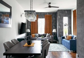 Ein modernes Wohnzimmer mit Essbereich, Deckenventilator und einem großen Fenster mit Vorhängen.