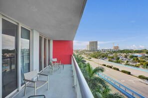 A balcony with a red wall, two chairs, and a view of a cityscape with buildings and a construction site. - APT w/ Canal View Condo Hallandale Resort Style (Hallandale Beach)