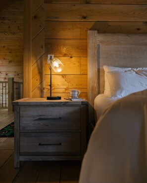 Ein Zimmer einer Holzhütte mit einem Bett, einem Nachttisch mit einer Lampe und einer Tasse auf dem Nachttisch.