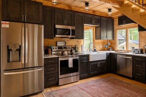 Une cuisine moderne dotée d’appareils électroménagers en acier inoxydable, de meubles de rangement aux couleurs sombres et d’un plafond en bois.